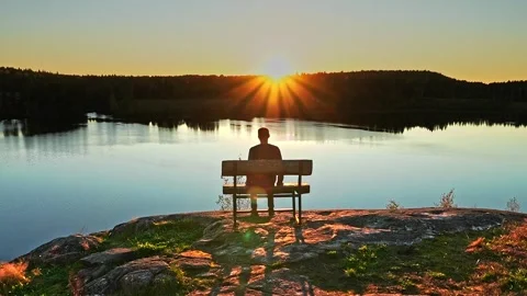 A man approaches, sits down on a bench on the cliff of river. Stock Footage 321618268