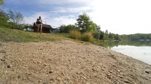 Man approaching the lakeside and stops to glance at the water Stock Footage 228671543