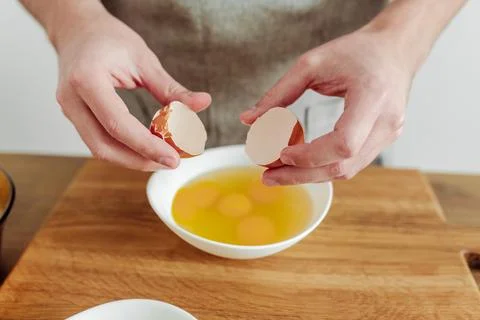 Man in apron cooking, in progress. Broken egg in hand Stock Photos