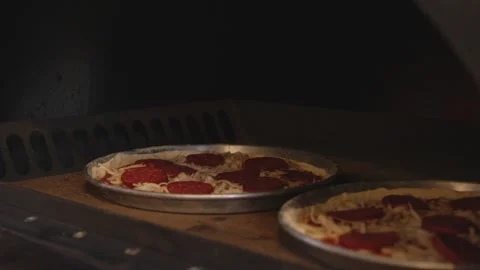A man in an apron is putting raw pizza into a wood-fired pizza oven. Cooking Stock Footage 259063472