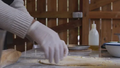 A man in an apron is rolling out pizza dough on a table sprinkled with flour. On Stock Footage 259063085