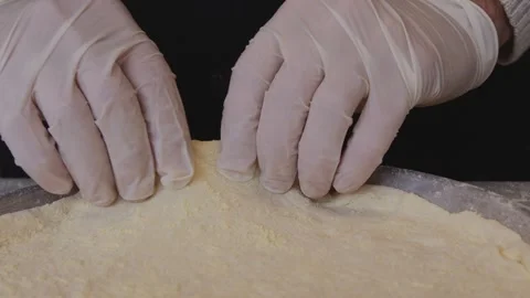 A man in an apron is rolling out pizza dough on a table sprinkled with flour. On Stock Footage 259063573