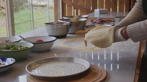 A man in an apron is rolling out pizza dough on a table sprinkled with flour. On Stock Footage 259179718