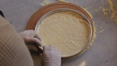 A man in an apron is rolling out pizza dough on a table sprinkled with flour. On Stock Footage 259405580