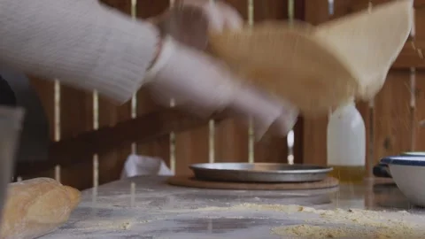 A man in an apron is rolling out pizza dough on a table sprinkled with flour. On Stock Footage 259405671