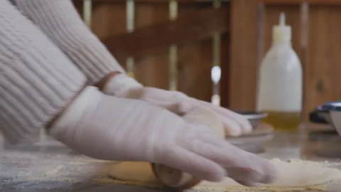A man in an apron is rolling out pizza dough on a table sprinkled with flour. On Stock Footage 259567155