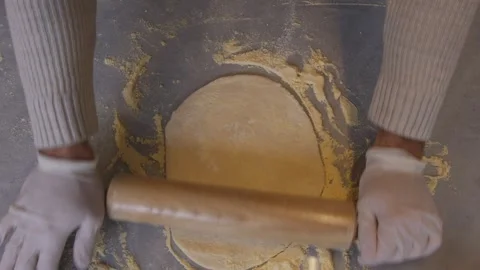 A man in an apron is spreading tomato paste on a pizza dough base on a table Stock Footage 258649184