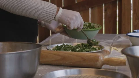 A man in an apron is spreading tomato paste on a pizza dough base on a table Stock Footage 258933209