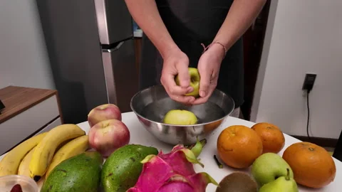 A man in an apron stands in front of a table with fruit, washing green apples in Stock Footage 317367796