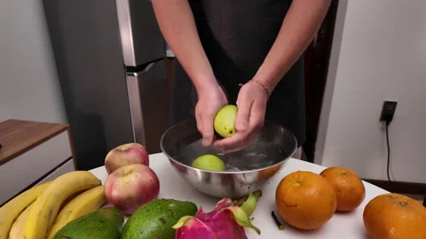 Man in an apron stands in front of a table with fruit, washing apples in a bowl Video stock 332200228