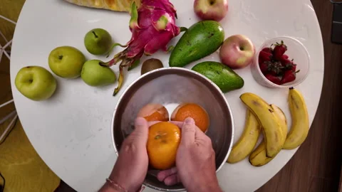 A man in an apron stands in front of a table with fruit, washing juicy mandarins Stock Footage 332203162