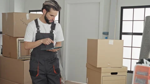 Man in apron taps tablet with finger while checking stacked moving boxes in.. Stock Footage 337371715