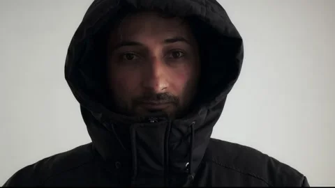 A man of Arab appearance in a black jacket with a hood pulled down over his eyes Video stock 240855631