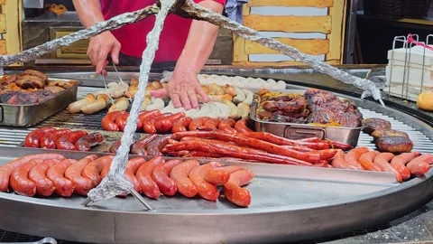 Man arranges sausages on a grill grate over coals at a German festival. 库存影片 340469301