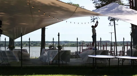Man arranging light bubbles garland at a summer terrace near the lake Stock Footage 59108635