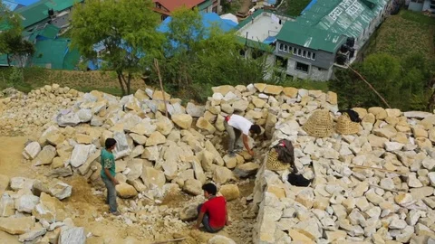 Man arranging rocks with two more men accompanying him at a high site in Nepal Stock Footage 77448133