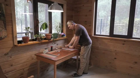 Man arranging wine glasses on dining table in cozy wooden cabin Stock Footage 336307497