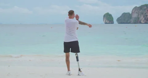 Man with artificial bionic leg doing body warm up before workout on a beach. Video stock 201366292