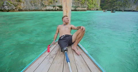 Man with artificial bionic leg relaxing by laying down on long tail boat front. Video stock 210729895