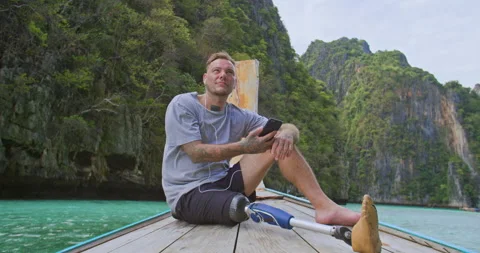 Man with artificial bionic leg sitting on boat front and listening music. Stock Footage 201366559