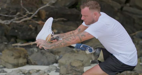 Man with artificial bionic leg takes off his running shoe after morning workout. Video stock 242444212