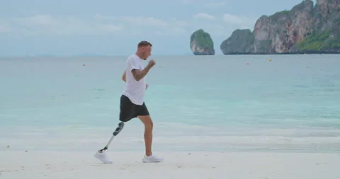 Man with artificial bionic legs running and jogging training on a beach. Video stock 201365854