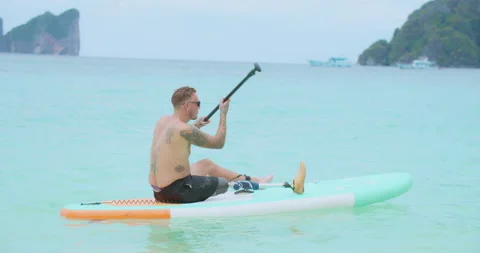 Man with artificial leg sitting on paddle board and sailing at tropical sea. Video stock 201370699