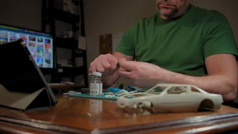 Man assembler plastic model of car in room at table according to drawings and Stock Footage 270451342