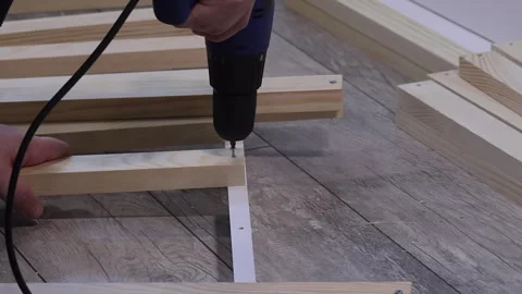A man assembles the base for mattresses. He attaches slats with screws usin.. Video stock 303856862