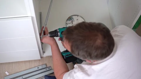 A man assembles a cabinet and tightens the guide with a screwdriver. Stock Footage 250956772