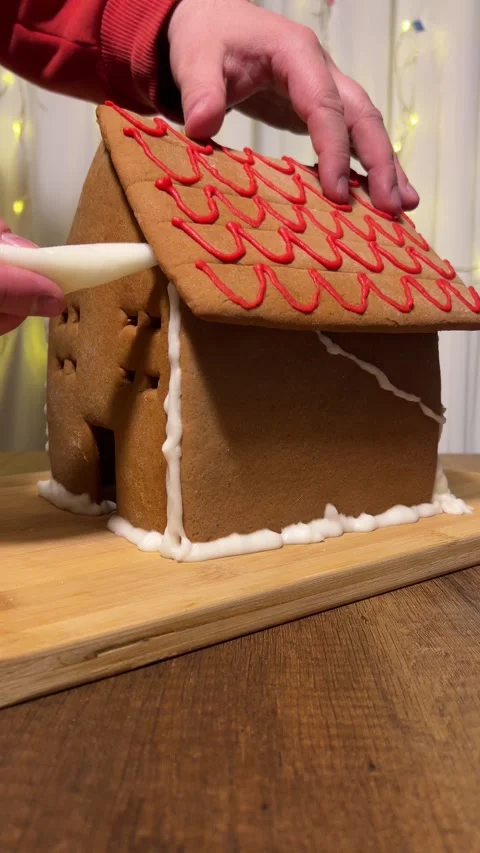 Man assembles gingerbread house on table, glues roof with white icing Stock Footage 304765951