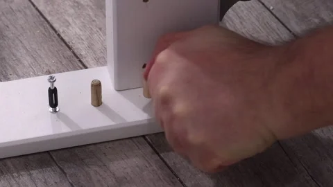 A man assembles an ottoman. Connects wooden elements using a cam dowel. Clo.. Stock Footage 303855464