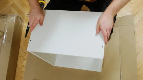 Man assembles square shelf of wooden plywood boards on floor Stock Footage 304399279