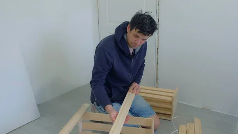 Man assembling collecting wooden rack furniture on floor at home house. Video stock 129590400