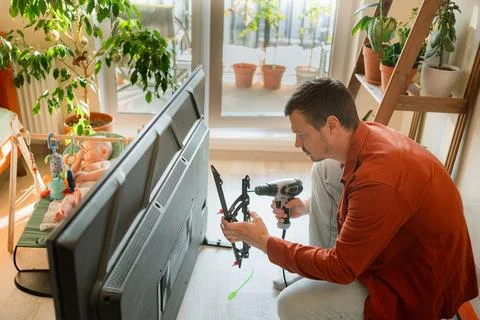 Man assembling a flat screen television mount with a power drill in a living Foto stock