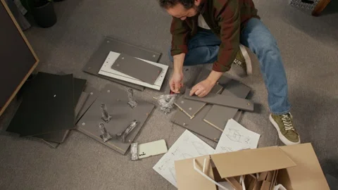 Man Assembling Flatpack Locker on Floor with Fixtures and Screwdriver Stock Footage 330512344