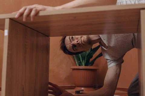 Man assembling new wooden table on floor in apartment 스톡 사진