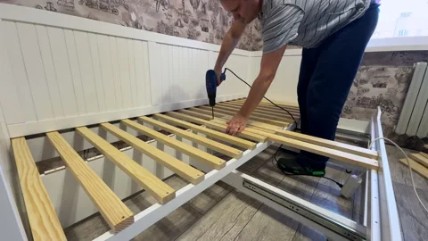A man is assembling an ottoman at home. He attaches wooden slats to the bas.. Stock Footage 304376419