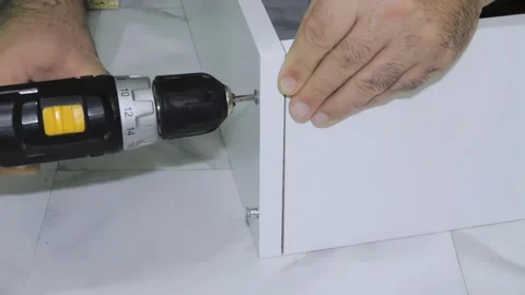 Man Assembling White Furniture with a Screwdriver. Home Furniture Assembly Stock Footage 293712435