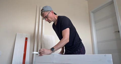 Man assembling white wooden shelving unit at home, measuring and drilling parts Stock Footage 314788945