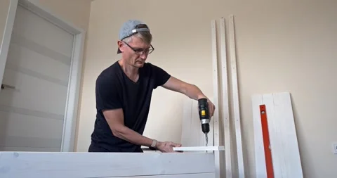 Man assembling white wooden shelving unit at home, measuring and drilling parts Stock Footage 314789090
