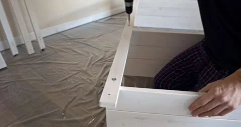 Man assembling white wooden shelving unit indoors using cordless screwdriver to Stock Footage 314789876