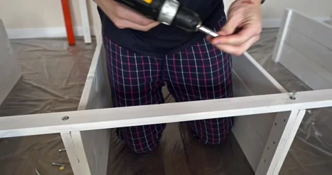 Man assembling white wooden shelving unit at home using cordless screwdriver to Stock Footage 314790298