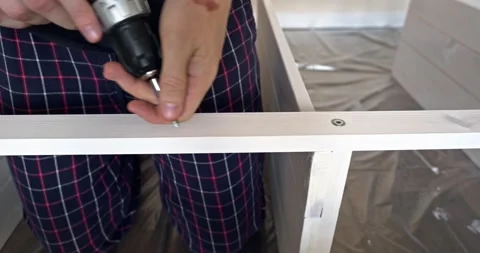 Man assembling white wooden shelving unit at home using cordless screwdriver to Stock Footage 314790945