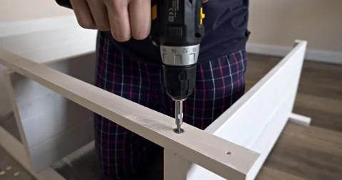 Man assembling white wooden shelving unit indoors using cordless screwdriver to Stock Footage 314791158