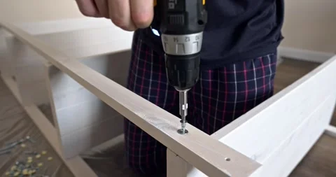 Man assembling white wooden shelving unit indoors using cordless screwdriver to Stock Footage 314791186