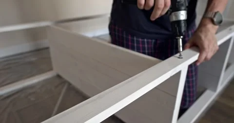 Man assembling white wooden shelving unit indoors using cordless screwdriver to Stock Footage 314791305