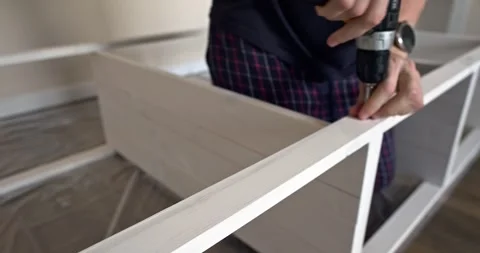 Man assembling white wooden shelving unit at home using cordless screwdriver to Stock Footage 314791371