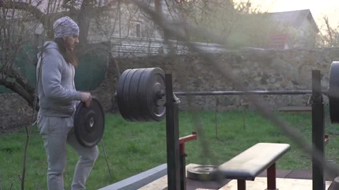 A man, an athlete, in the early spring, trains, prepares the barbell Stock Footage 131060347