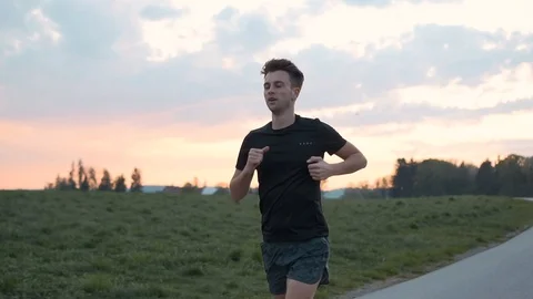 Man athlete running between meadows with colourful sky, slow motion Stock Footage 129610582
